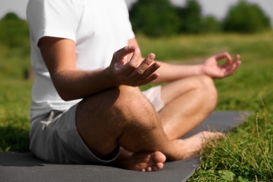 Man practicing yoga on mat outdoors, closeup. Lotus pose