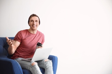 Photo of Young blogger with laptop sitting in armchair against light wall