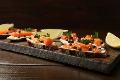 Photo of Tasty canapes with salmon, capers, lemon and cream cheese on wooden table, closeup