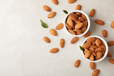 Tasty organic almond nuts in bowls and space for text on table, top view