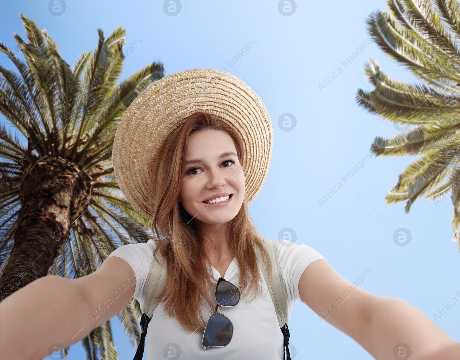 Image of Beautiful woman in straw hat taking selfie near tropical palms
