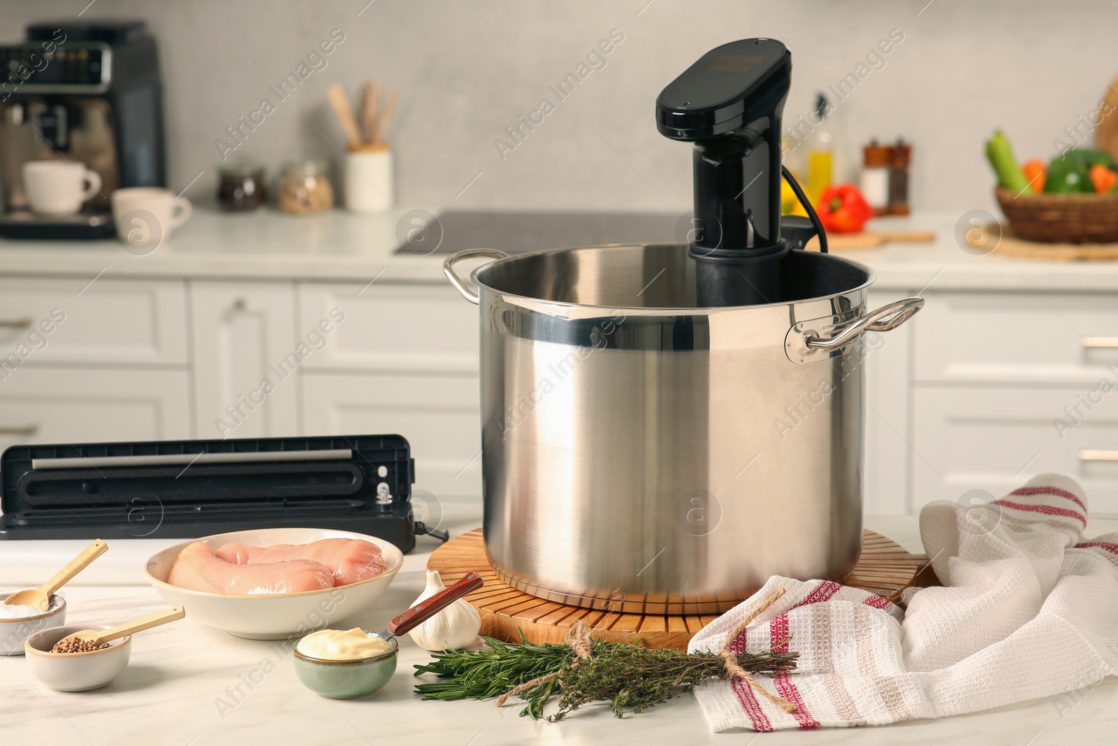 Photo of Thermal immersion circulator in pot, sealer for vacuum packing and ingredients on table in kitchen. Sous vide cooking