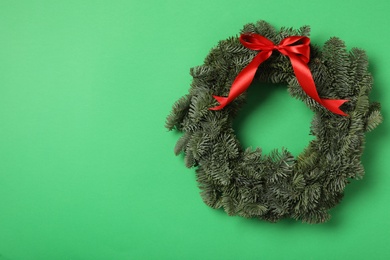 Photo of Christmas wreath made of fir tree branches with red ribbon on green background, space for text