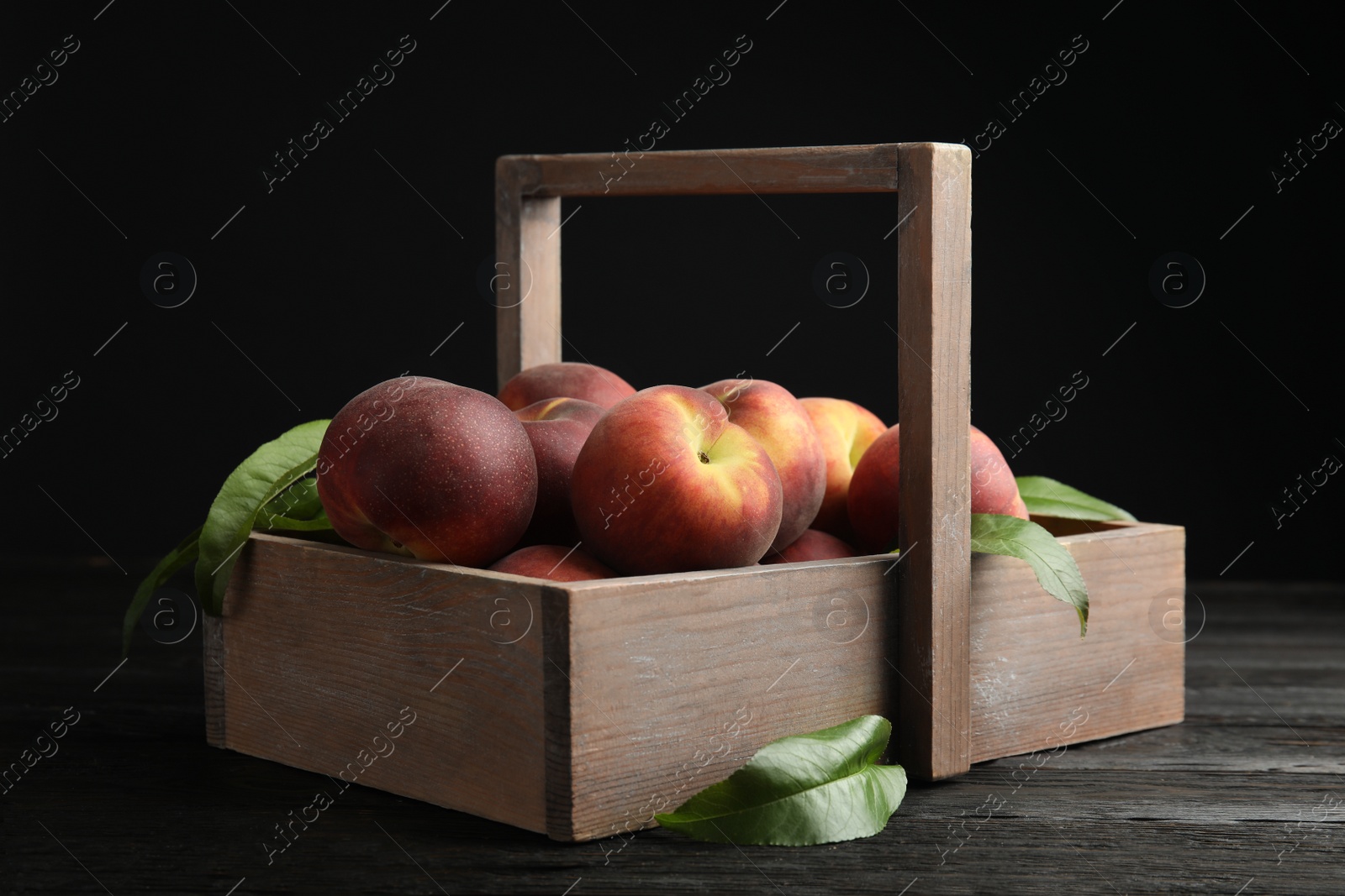 Photo of Wooden crate with tasty peaches on table against black background