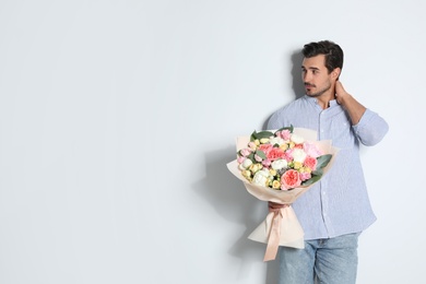 Photo of Young handsome man with beautiful flower bouquet on light background, space for text