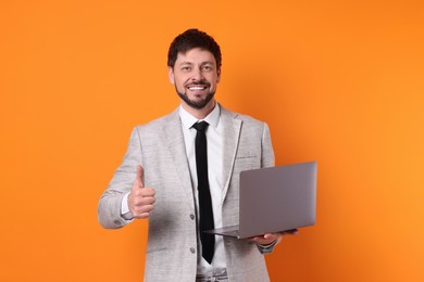Photo of Happy man with laptop showing thumb up on orange background