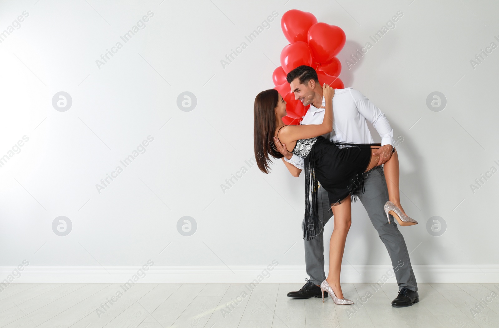 Photo of Beautiful couple with heart shaped balloons dancing on light background, space for text