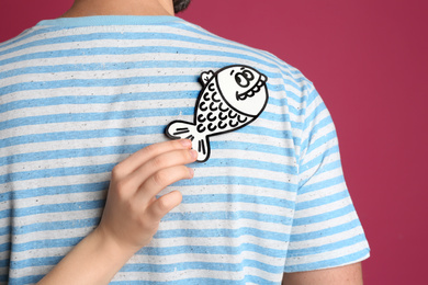 Woman sticking paper fish to friend's back on pink background. April fool's day