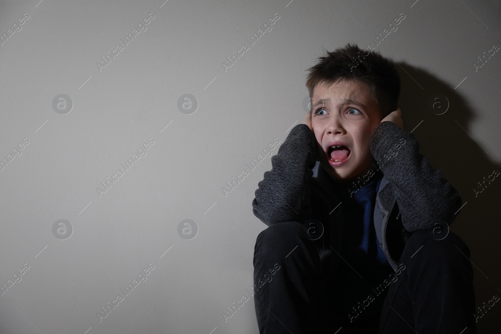 Photo of Scared little boy near beige wall, space for text. Domestic violence concept