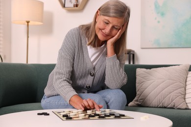 Happy senior woman playing checkers at home