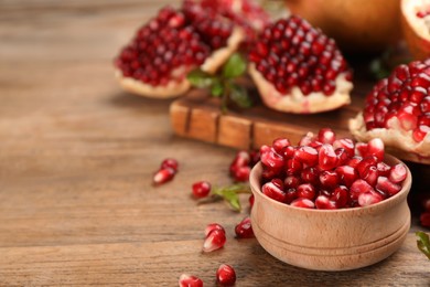 Photo of Delicious ripe pomegranate kernels in bowl on wooden table. Space for text