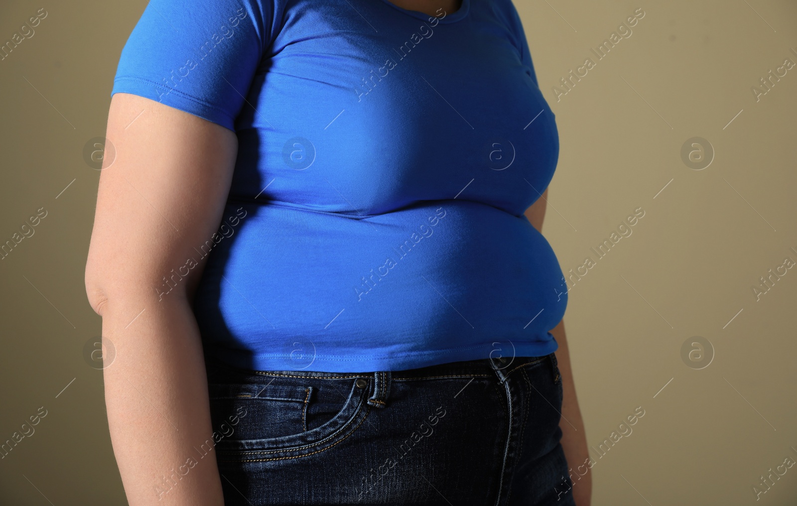 Photo of Overweight woman in tight t-shirt on light brown background, closeup