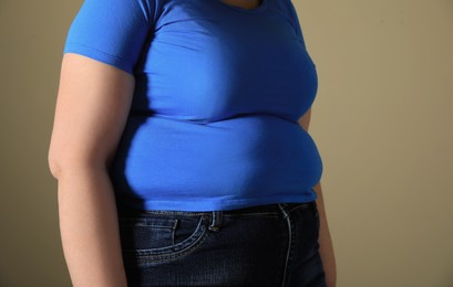 Photo of Overweight woman in tight t-shirt on light brown background, closeup