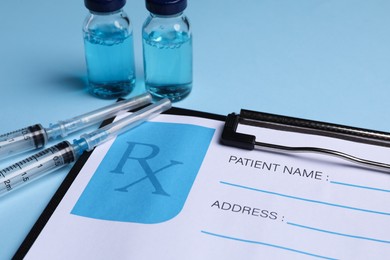 Photo of Clipboard with medical prescription form, syringes and glass vials on light blue background, closeup