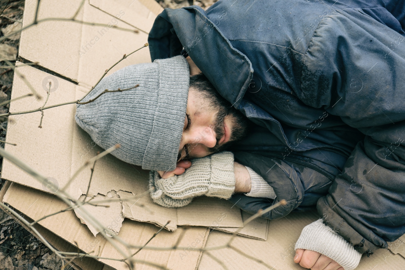 Photo of Poor homeless man lying on cardboard outdoors