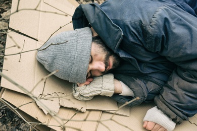 Poor homeless man lying on cardboard outdoors