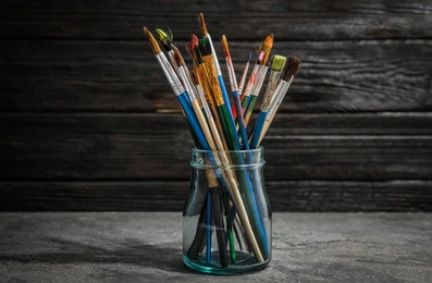 Jar with paint brushes on table against wooden background