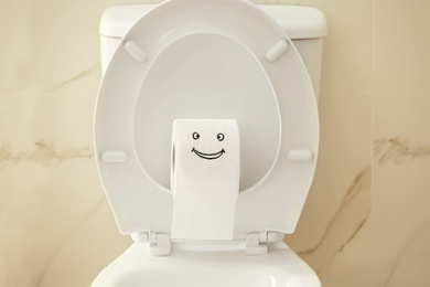 Roll of paper with funny face on toilet bowl in bathroom