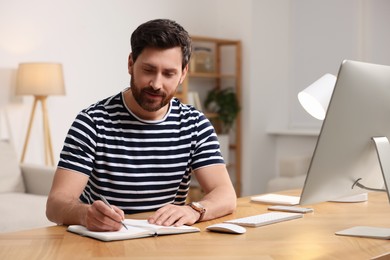 Photo of Home workplace. Man taking notes near computer at wooden desk in room