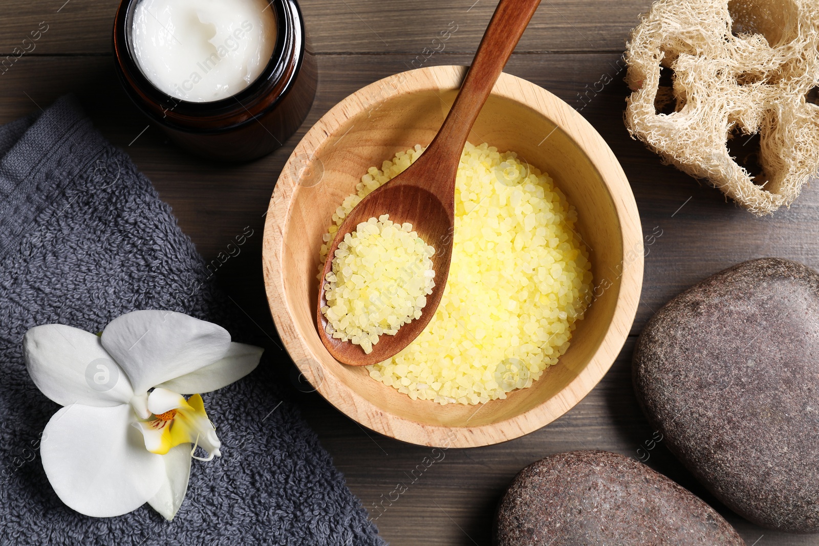 Photo of Natural sea salt in bowl, sponge, spa stones, towel and beautiful orchid on wooden table, flat lay