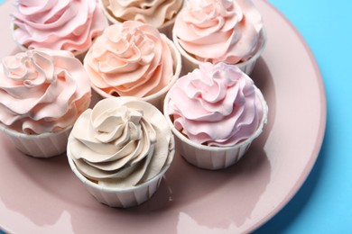 Photo of Plate with tasty cupcakes on light blue background, closeup