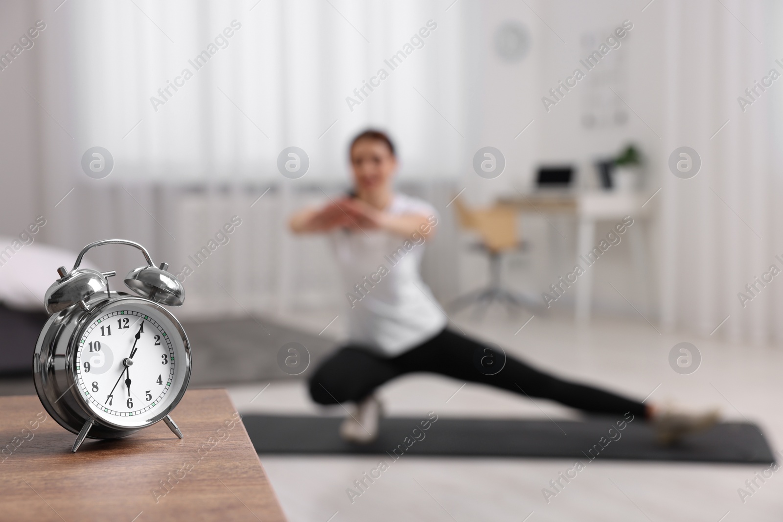 Photo of Morning routine. Alarm clock on wooden table and woman doing exercise, selective focus. Space for text