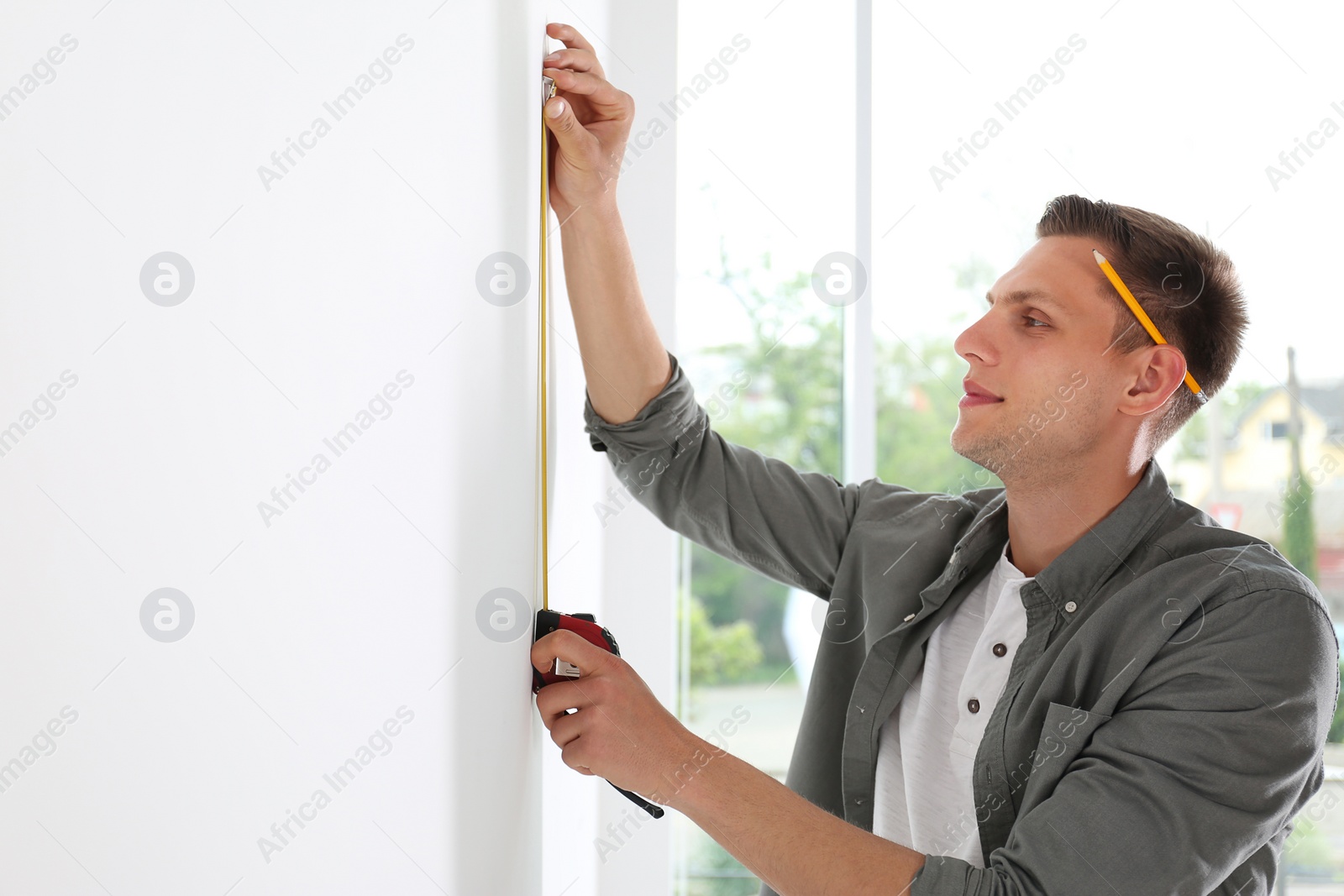 Photo of Young man working with measuring tape near white wall. Space for text