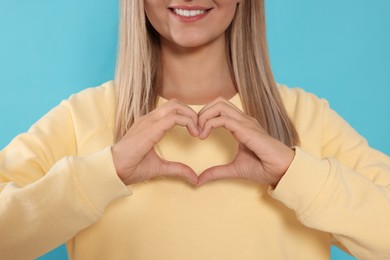 Happy volunteer making heart with her hands on light blue background, closeup