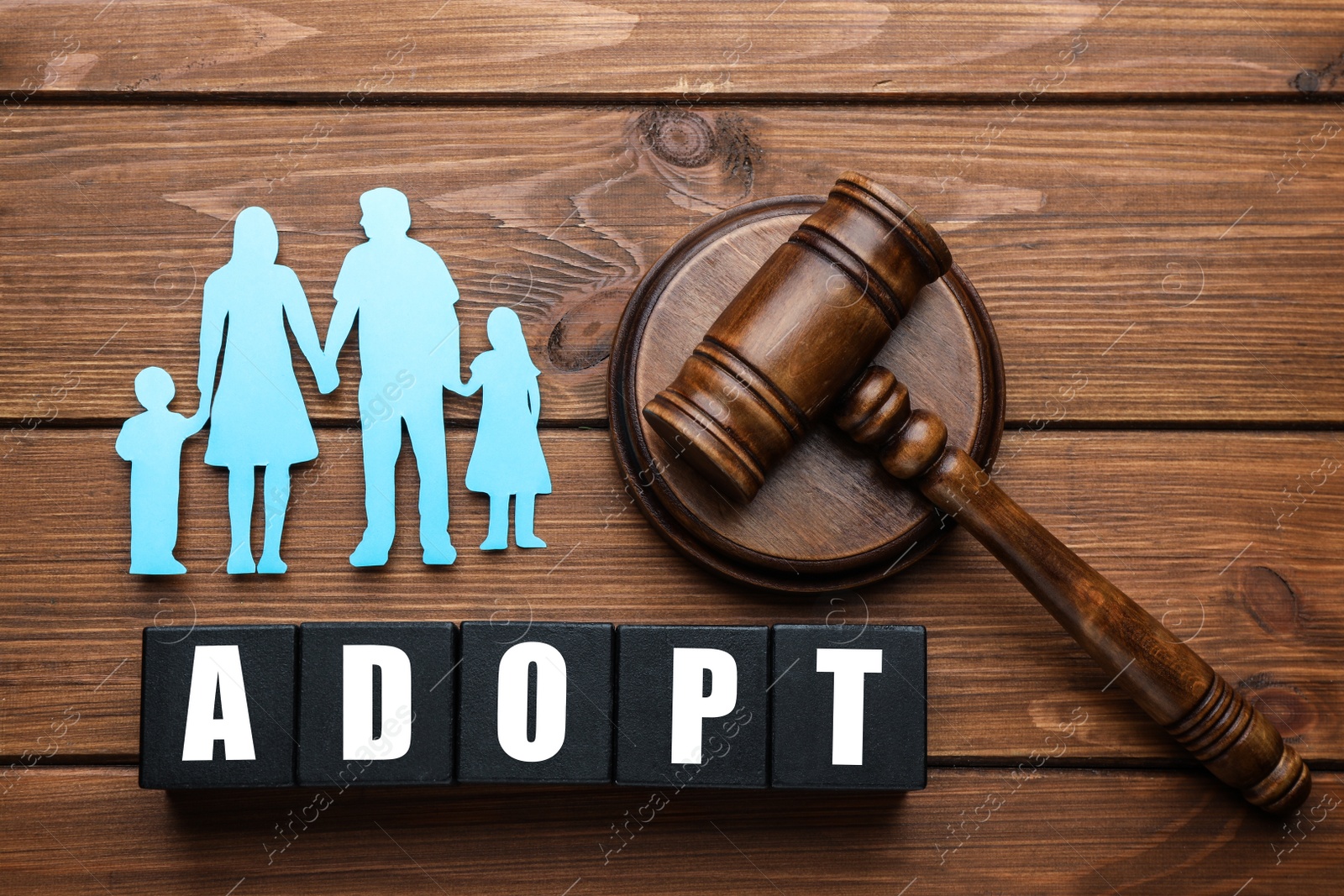 Photo of Family figure, gavel and word Adopt made of cubes on wooden table, flat lay