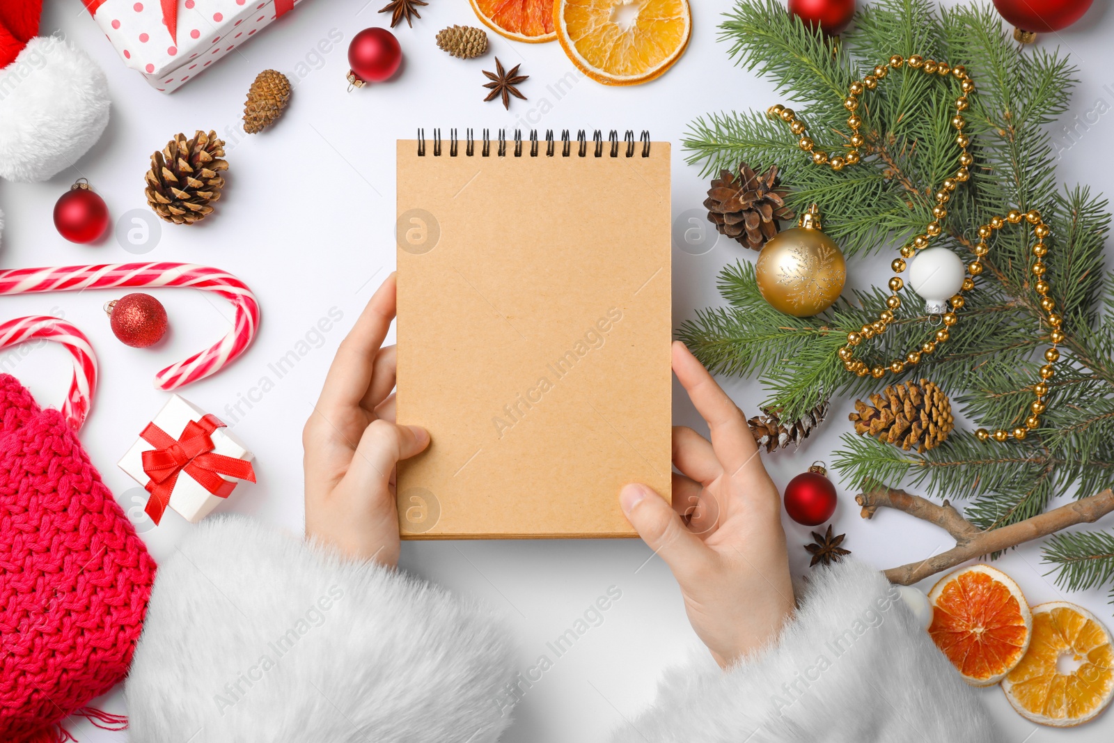 Photo of Santa Claus holding notebook and Christmas decor on white background, top view