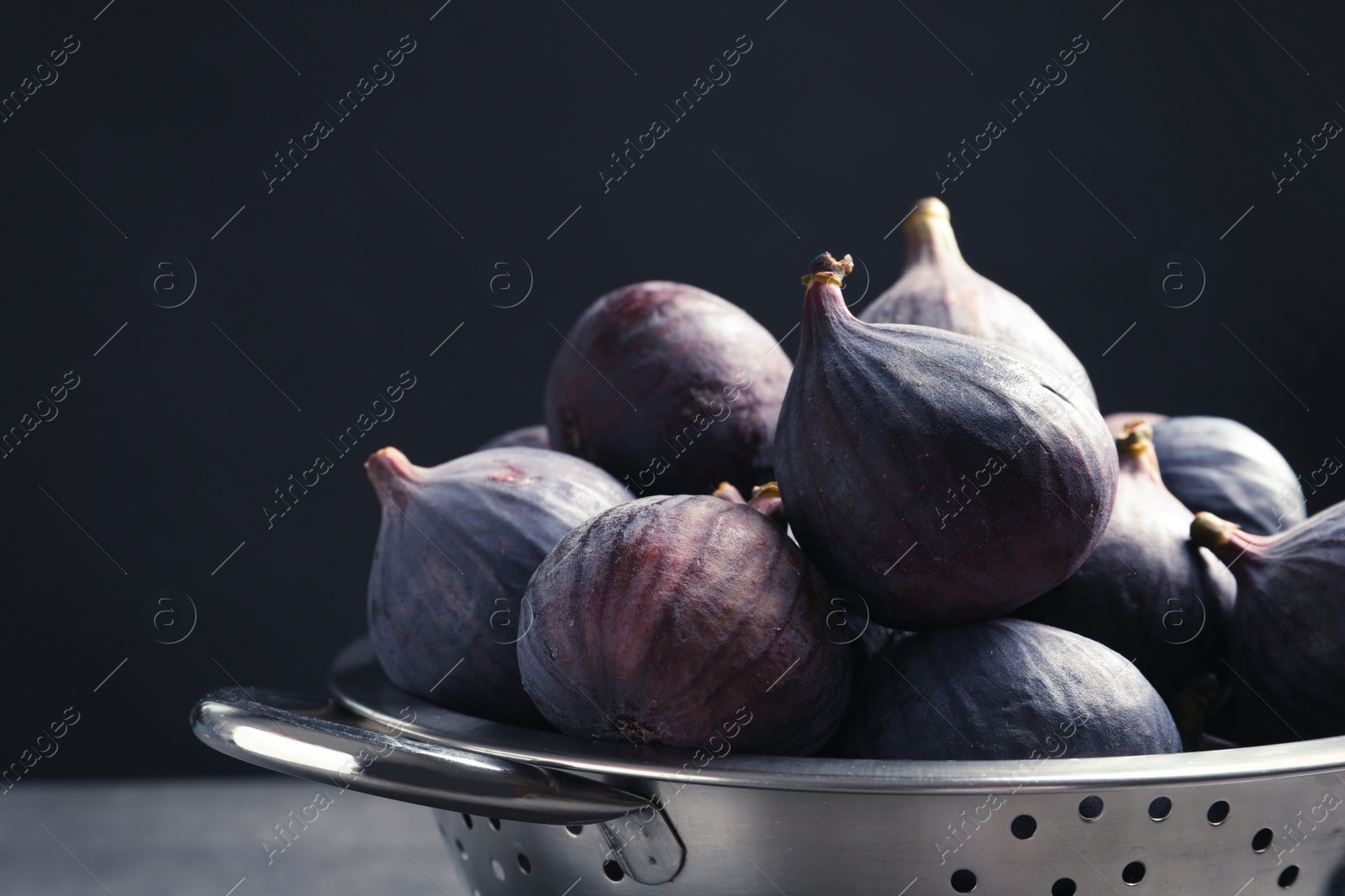 Photo of Colander with fresh ripe figs against black background, closeup