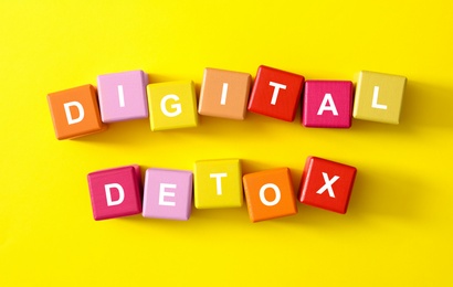 Photo of Colorful cubes with phrase DIGITAL DETOX on yellow background, flat lay