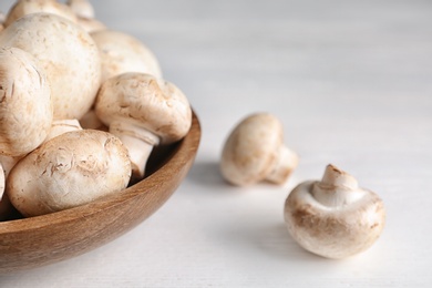 Bowl with fresh champignon mushrooms on wooden table, closeup. Space for text