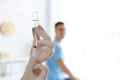 Photo of Doctor holding ampule with vaccine and syringe for patient in clinic, closeup
