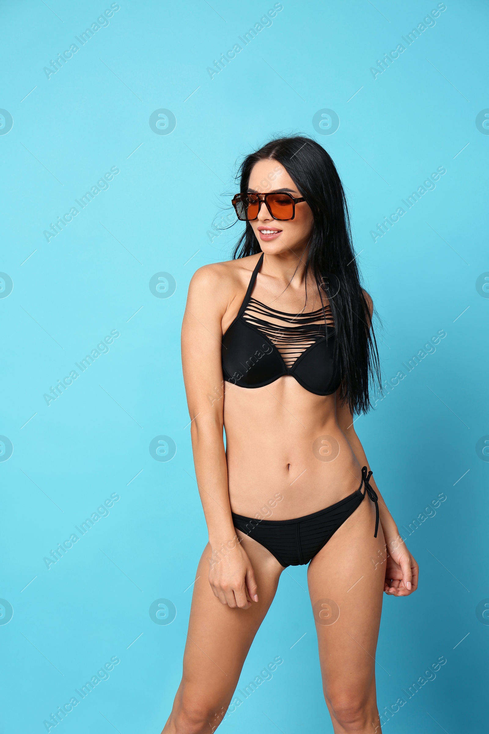 Photo of Beautiful young woman in black bikini with sunglasses on light blue background