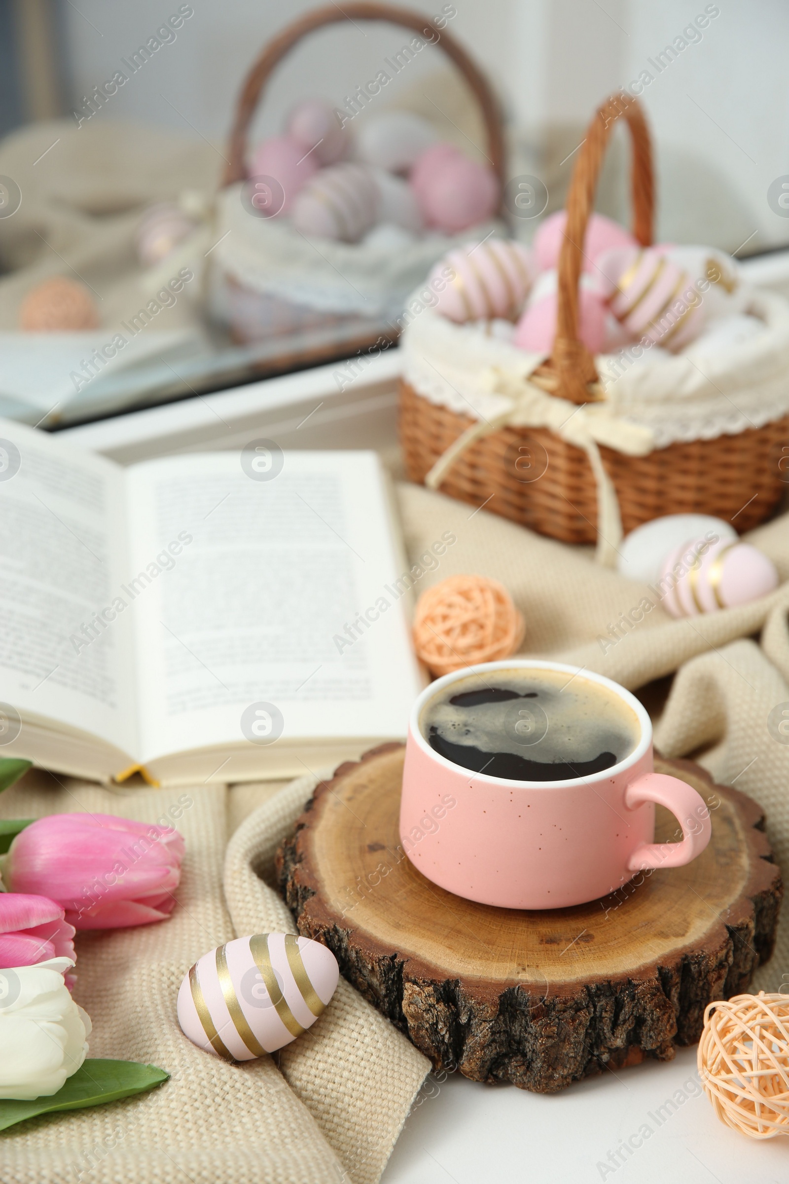 Photo of Easter decorations. Cup of coffee, painted eggs, tulips and book on windowsill