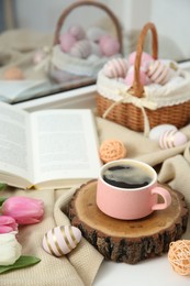 Easter decorations. Cup of coffee, painted eggs, tulips and book on windowsill