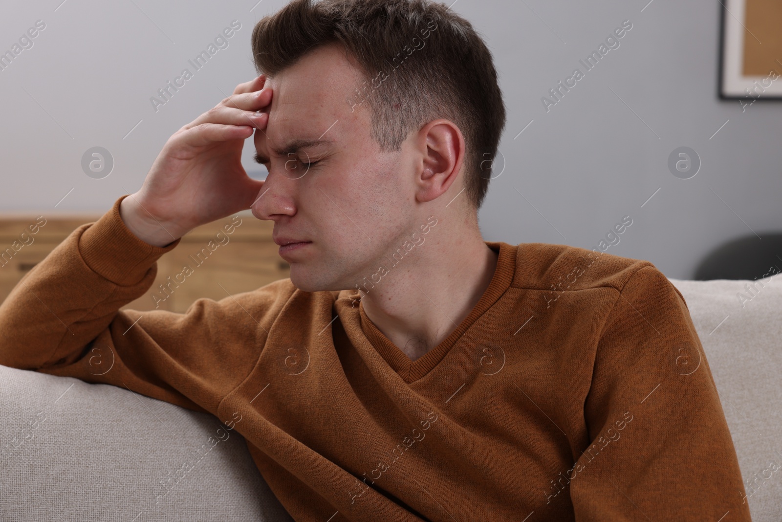 Photo of Sad man suffering from headache on sofa indoors