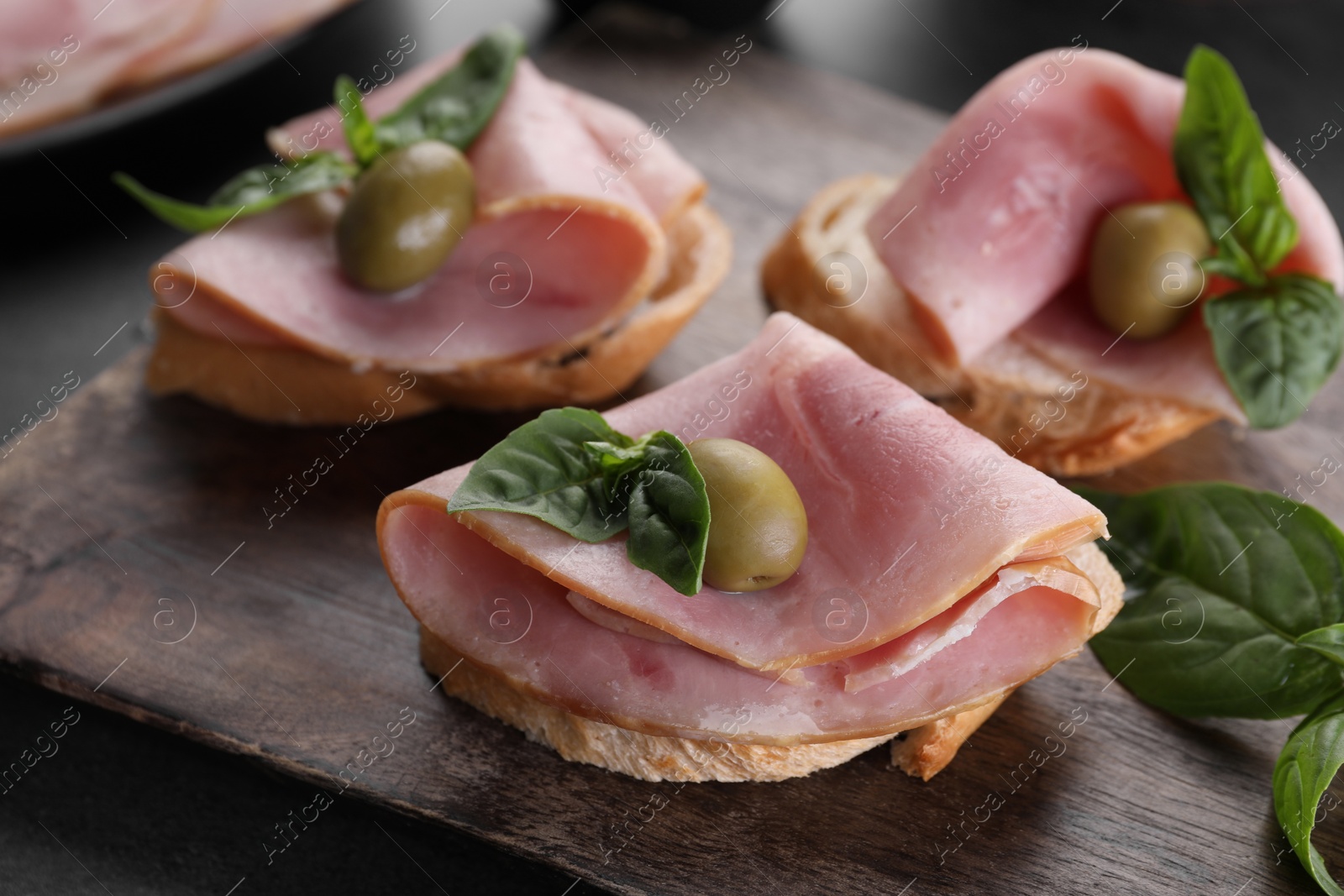 Photo of Delicious sandwiches with ham, basil and olives on table, closeup