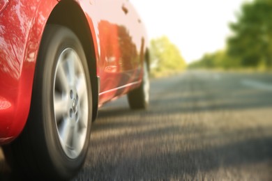 Red car driving on road outdoors, closeup with motion blur effect. Space for text