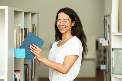 Young woman putting book on shelf in library