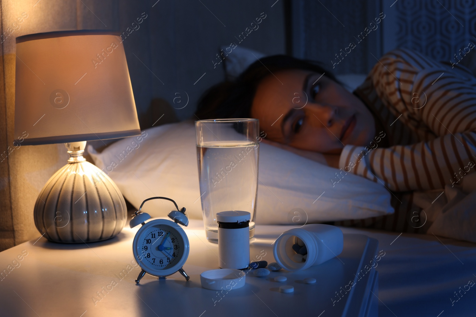 Photo of Mature woman suffering from insomnia in bed at night, focus on nightstand with pills, alarm clock and water