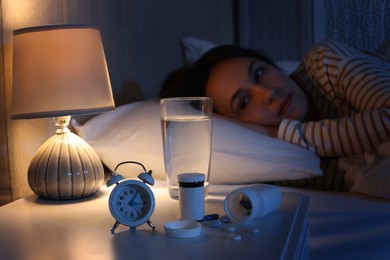 Photo of Mature woman suffering from insomnia in bed at night, focus on nightstand with pills, alarm clock and water