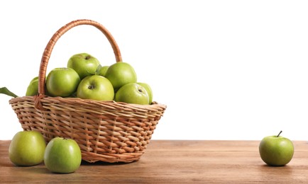 Photo of Ripe green apples in wicker basket on wooden table against white background. Space for text