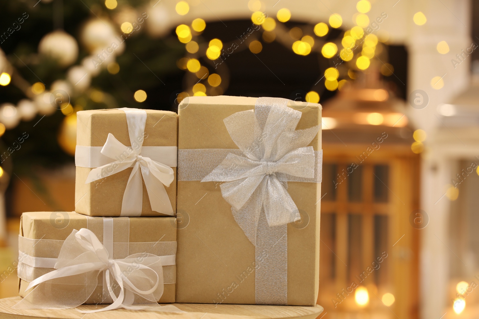 Photo of Beautifully wrapped gift boxes on wooden table against blurred festive lights. Christmas celebration