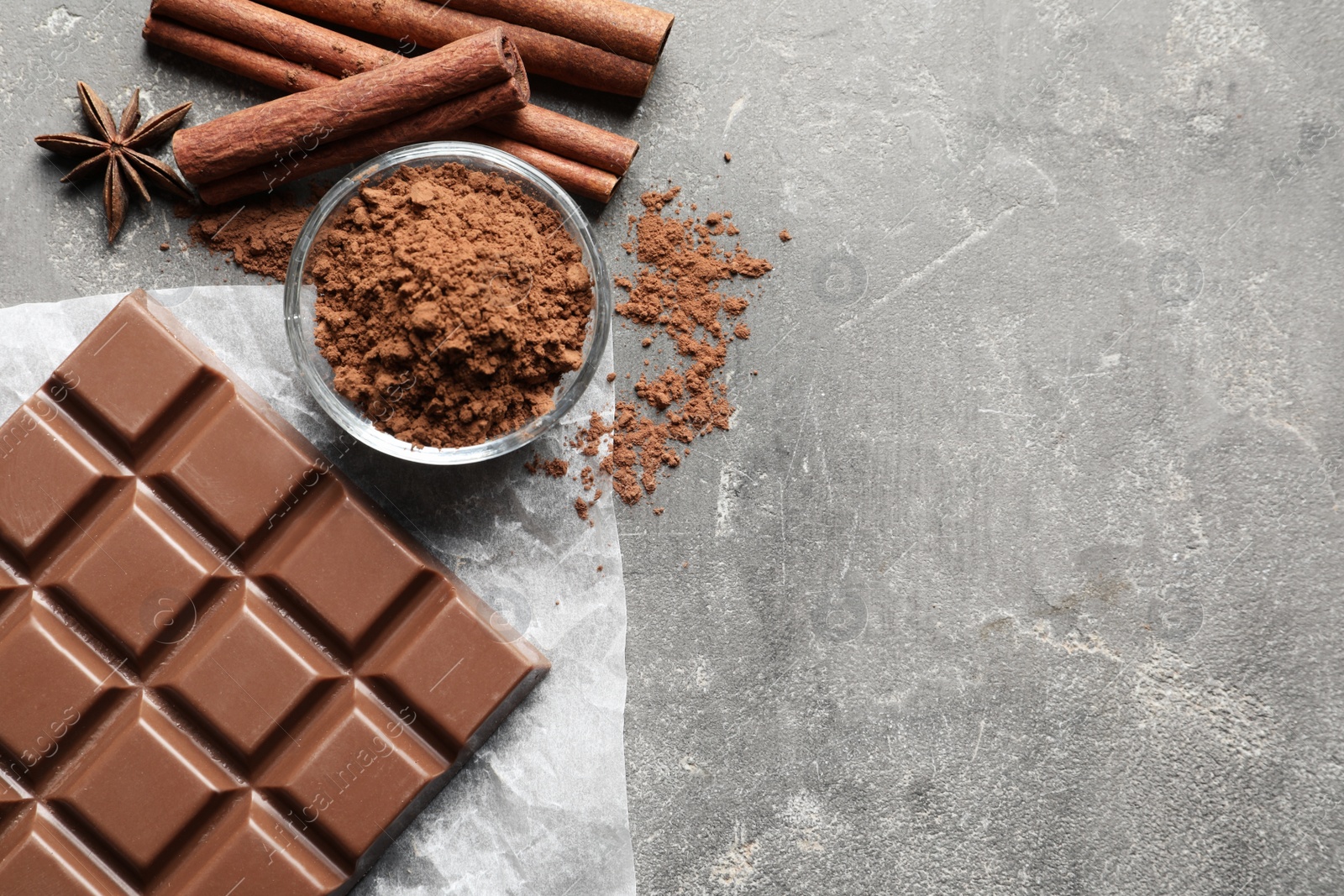 Photo of Chocolate bar and cocoa powder on grey background, flat lay. Space for text