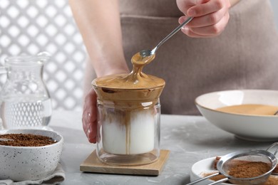 Photo of Woman making dalgona coffee at light gray table, closeup