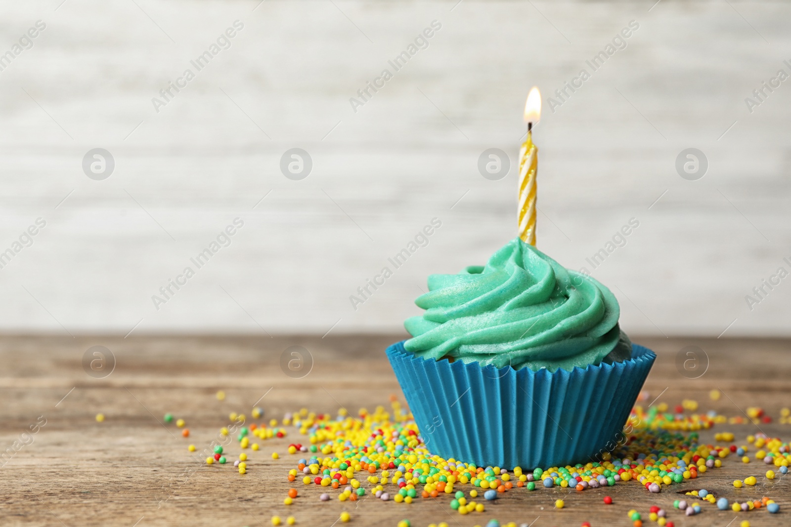 Photo of Delicious birthday cupcake with cream and burning candle on wooden table. Space for text