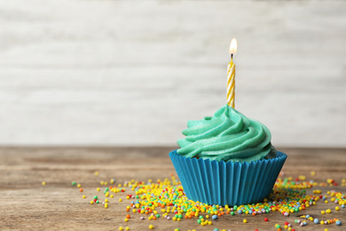 Delicious birthday cupcake with cream and burning candle on wooden table. Space for text