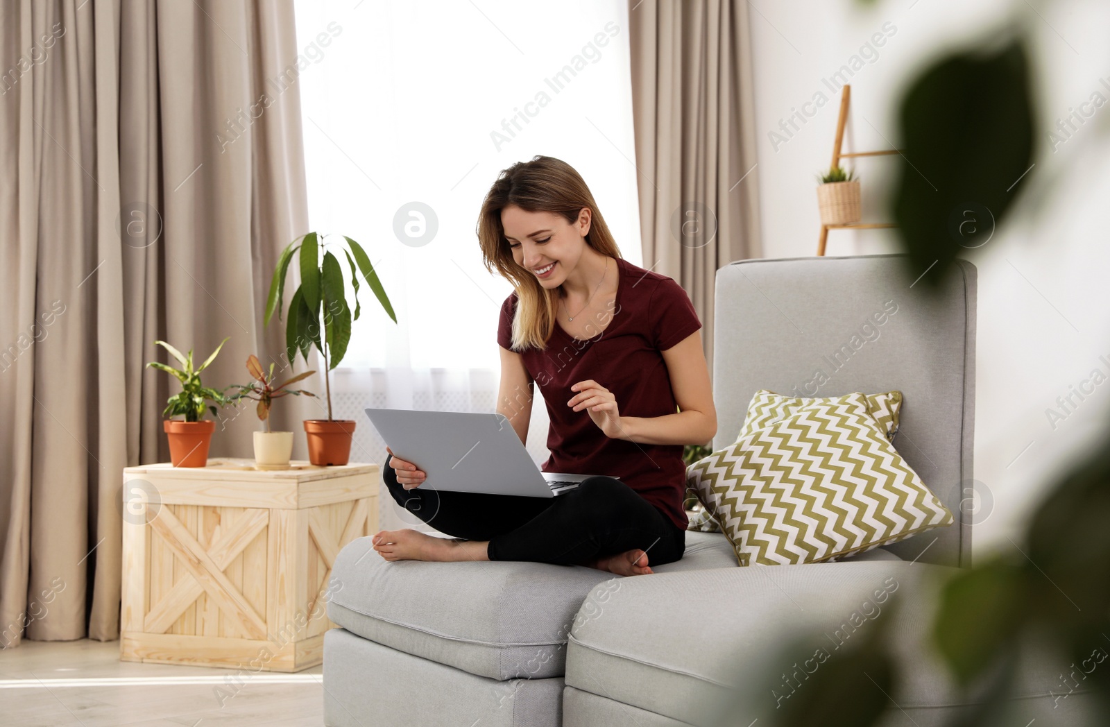 Photo of Young woman using laptop at home. Trendy room interior with plants